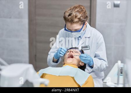 Portrait d'une jeune femme dentiste portant un masque tout en travaillant avec une patiente en clinique Banque D'Images