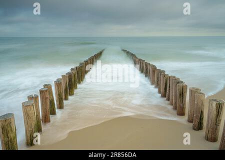 Brise-vagues sur la plage de Domburg aux pays-Bas. Photo longue exposition avec des vagues dynamiques se brisant sur le rivage sur des poteaux en bois Banque D'Images