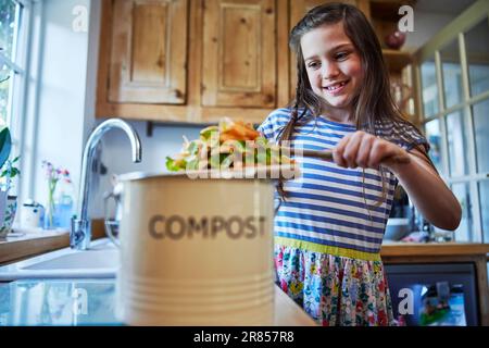 Fille dans la cuisine faisant du compost raclant les restes de légumes dans le bac Banque D'Images