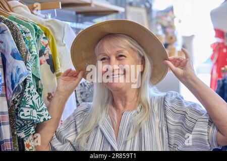 Femme âgée achetant des vêtements durables d'occasion à la boutique de charité d'occasion ou à la boutique de Thrift essayant sur le chapeau Banque D'Images