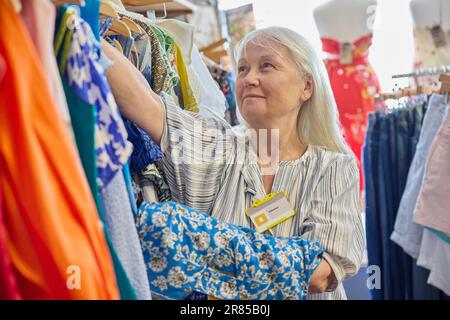 Femme bénévole senior travaillant dans la boutique de bienfaisance ou dans le magasin Thrift vendant des vêtements d'occasion et durables Banque D'Images