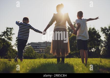 Une mère heureuse joue avec ses fils dans le parc. Ils tiennent les mains et profitent du coucher du soleil. Banque D'Images