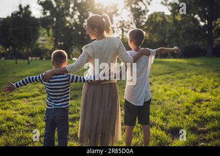 Une mère heureuse joue avec ses fils dans le parc. Ils tiennent les mains et profitent du coucher du soleil. Banque D'Images