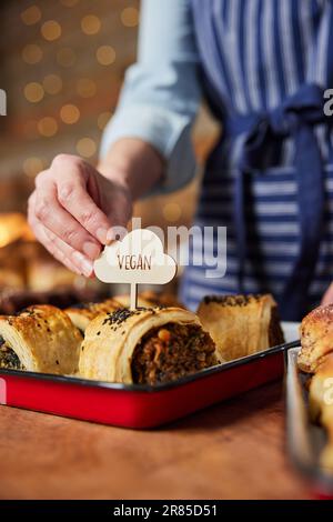 Assistant commercial de la boulangerie plaçant l'étiquette de Vega dans un rouleau de produits salés fraîchement cuits Banque D'Images