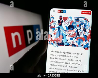 Personne tenant un téléphone cellulaire avec le site Web de l'organisation médiatique National public radio (NPR) à l'écran avec logo. Concentrez-vous sur le centre de l'écran du téléphone. Banque D'Images