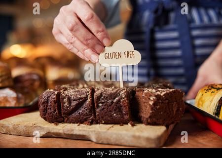 Assistant commercial de la boulangerie mettant une étiquette sans gluten dans des brunes fraîchement cuites au four Banque D'Images