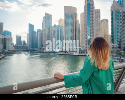 Une jeune femme en costume vert marche dans les rues de Dubaï, quartier de la marina de Dubaï. Concept de voyage aux Émirats arabes Unis. l'idée d'un expatrié réussi, d'un déménagement dans un autre pays, d'un visa de travail Banque D'Images