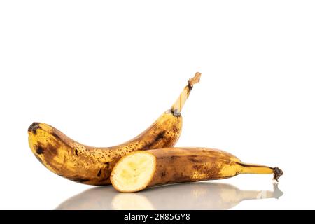 Une banane entière et une banane à moitié surmûre avec un couteau sur un plan de cuisine en bois, macro, isolée sur fond blanc. Banque D'Images