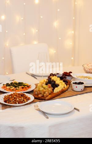 Table festive décorée de nappes blanches et dorées, avec assortiment de salades, plateau de fromages, saumon fumé, verres avec vin, bokeh l Banque D'Images