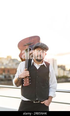 Portrait d'un musicien regardant la caméra tout en tenant sa guitare sur son épaule Banque D'Images