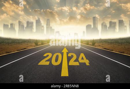 Année 2024 écrit sur route asphaltée plate. Route vide vers la ville et lever du soleil sur les gratte-ciel. 2024 objectifs du nouvel an Banque D'Images