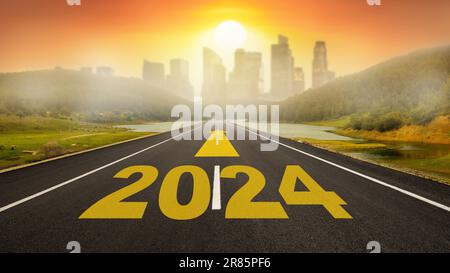 Année 2024 écrit sur route asphaltée plate. Route vide vers la ville et lever du soleil sur les gratte-ciel. 2024 objectifs du nouvel an Banque D'Images