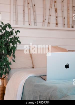 MacBook sur le lit dans la maison de campagne chambre à coucher arrière-plan intérieur. Ordinateur portable en aluminium argenté au lit près d'un arbre verin dans une maison de campagne scandinave Banque D'Images