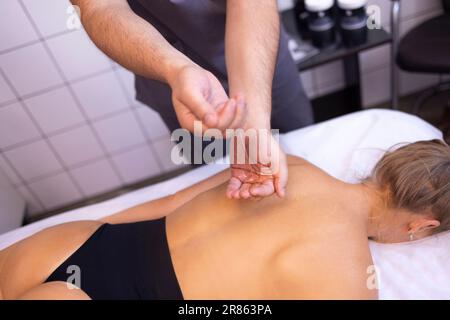 Gros plan des mains du masseur avec de l'huile avant le début de la session dans la clinique ou le salon de beauté. La jeune femme est allongée sur une table de massage en attendant le massage du bac Banque D'Images