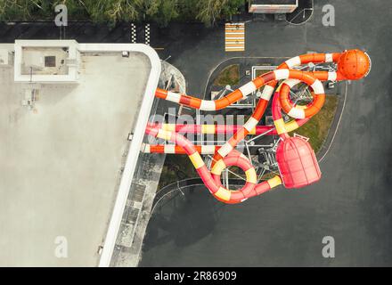 Vue aérienne en haut vers le bas des toboggans colorés et sinueux d'une attraction dans un parc aquatique intérieur. Bâtiment moderne du centre de divertissement avec parc aquatique Banque D'Images