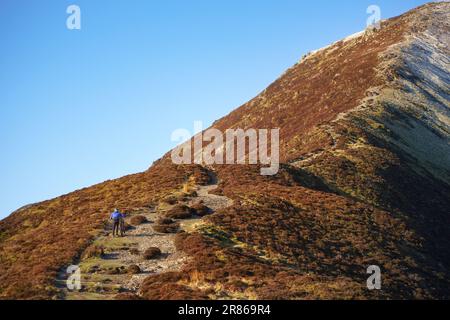 Un motard de montagne poussant leur vélo sur la piste jusqu'au sommet de Grisedale en hiver dans le district des lacs anglais, au Royaume-Uni. Banque D'Images