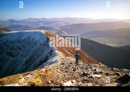 Une randonneur femelle et son chien marchant vers le sommet de Sail depuis Crag Hill en hiver dans le district des lacs anglais, au Royaume-Uni. Banque D'Images