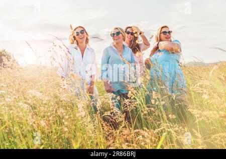 Portrait de quatre femmes souriantes et souriantes lors de la marche en plein air à côté d'une colline d'herbe verte. Ils regardent la caméra. L'amitié de la femme Banque D'Images