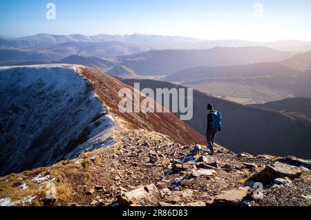 Une randonneur femelle et son chien marchant vers le sommet de Sail depuis Crag Hill en hiver dans le district des lacs anglais, au Royaume-Uni. Banque D'Images