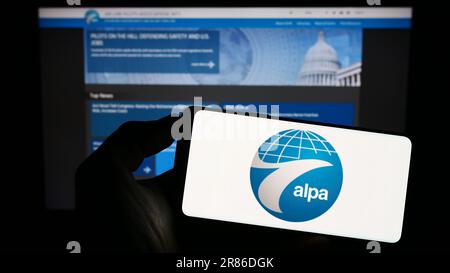 Personne tenant un téléphone portable avec le logo de l'Association internationale des pilotes de ligne aérienne (ALPA) à l'écran devant la page Web. Mise au point sur l'affichage du téléphone. Banque D'Images