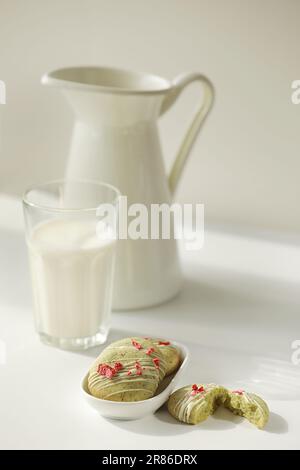 Composition avec biscuits maison au pain d'épice à la menthe avec matcha et fraises sublimées dans une assiette, verre de lait, pot et fleurs sauvages dans un vase sur la ba Banque D'Images