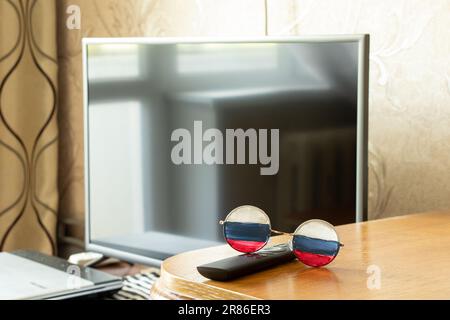 Le drapeau de la Russie sur les lunettes qui se trouvent sur la table à la maison contre le fond de la télévision, la Russie et la propagande de la télévision, mensonges et tromperie Banque D'Images