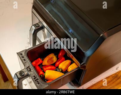 Friteuse à air à deux compartiments avec un tiroir ouvert pour révéler les poivrons rouges et jaunes rôtisant les bébés. Banque D'Images