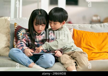 deux enfants asiatiques frère et soeur assis sur un canapé de famille à la maison jouant à un jeu d'ordinateur à l'aide d'une tablette numérique Banque D'Images