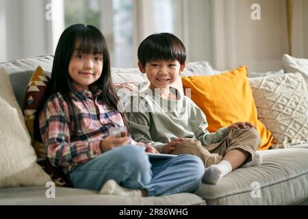 portrait de deux enfants asiatiques frère et soeur assis sur un canapé de famille à la maison regardant l'appareil photo sourire Banque D'Images