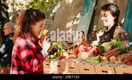 Bonne femme regardant les pommes juteuses à acheter sur le marché agricole, en vérifiant les produits sains sur le marché local stand. Femme clint fournisseur invité, produits bio frais. Prise de vue à main levée. Banque D'Images