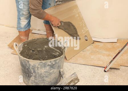 L'employé répandant le mélange d'adhésif sur les carreaux avec une spatule, gros plan Banque D'Images