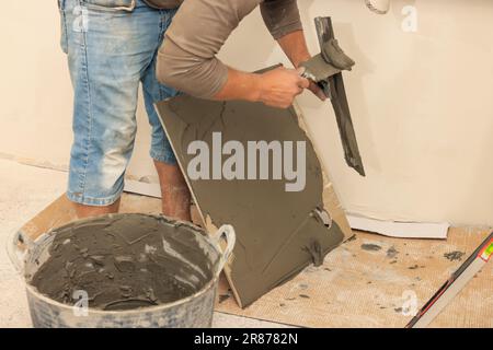 L'employé répandant le mélange d'adhésif sur les carreaux avec une spatule, gros plan Banque D'Images