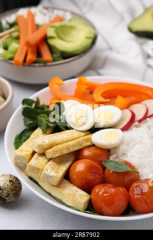 Délicieux bol à lait avec basilic, légumes, œufs et tofu sur table gris clair Banque D'Images