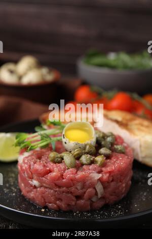 Savoureux steak tartare de bœuf servi avec des œufs de caille et d'autres accompagnements sur une assiette noire, en gros plan Banque D'Images