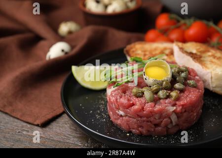 Savoureux steak tartare de bœuf servi avec des œufs de caille et d'autres accompagnements sur une table en bois, à proximité Banque D'Images