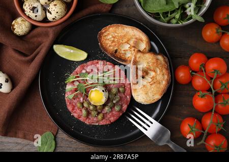 Savoureux steak tartare de bœuf servi avec des œufs de caille et d'autres accompagnements sur une table en bois, plat Banque D'Images