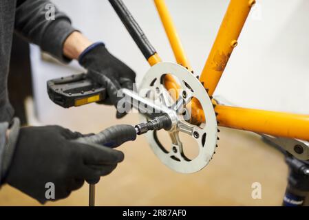 Entretien d'un vélo : mains d'une personne méconnaissable utilisant des gants pour démonter les pédales d'un vélo orange dans son atelier de réparation. Banque D'Images