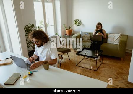 Couple marié indépendants assis dans la salle de séjour avec des ordinateurs portables et travaillant à domicile Banque D'Images