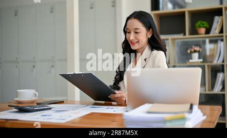 Une femme d'affaires ou une gestionnaire asiatique attirante du millénaire lit les rapports d'affaires à son bureau. Banque D'Images