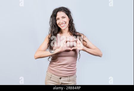 Jeune femme souriante qui prend la forme du cœur avec ses mains. Jeune fille faisant la forme de coeur avec ses mains, bonne fille faisant la forme de coeur avec les mains isolées Banque D'Images