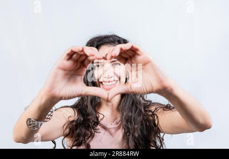 Bonne fille en forme de coeur avec les mains isolées. Jeune femme souriante qui prend la forme du cœur avec ses mains. Jeune fille faisant la forme du coeur avec ses mains Banque D'Images