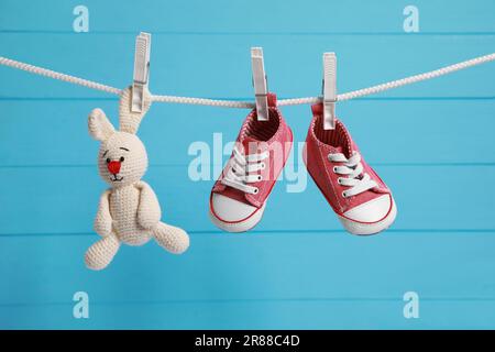 Les adorables sneakers pour bébé et le jouet en crochet séchant sur la ligne de lavage contre le mur en bois bleu clair Banque D'Images