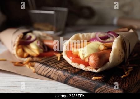 Délicieux emballage de pita avec des saucisses, des légumes et des pommes de terre frites sur une table en bois blanc, en gros plan Banque D'Images