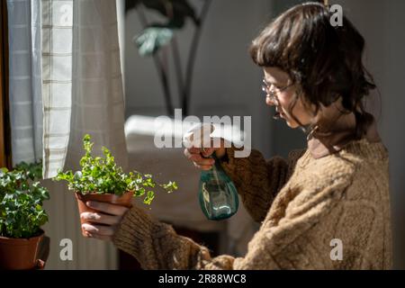 Adolescente prenant soin des plantes de maison à la maison, embuant les feuilles de plantes d'intérieur en pot Banque D'Images