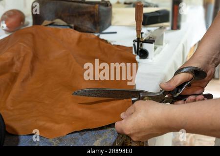 Artisan coupant le cuir avec de grandes vieilles ciseaux dans son atelier, matériel pour créer des sacs, ceintures, vêtements ou sellerie copie espace, choisi focus, na Banque D'Images