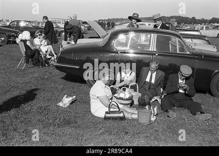 Classe ouvrière classe supérieure, chapeau haut de gamme et queues, chapeau en tissu et tuyau, son Derby Day. Les Londoniens descendent pour une journée aux courses, profitent d'un pique-nique en plein air dans le parking, à l'abri de la brise et au soleil, ils se penchent contre un Jaguar de retour. Epsom Downs, Surrey, Angleterre 3 juin 1970. ANNÉES 1970 ROYAUME-UNI HOMER SYKES Banque D'Images