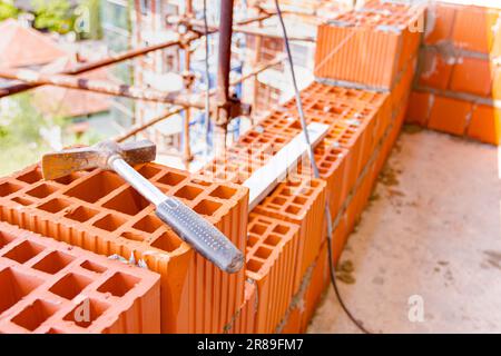 Marteau de maçon utilisé placé sur bloc de céramique rouge, mur de briques de construction. Banque D'Images