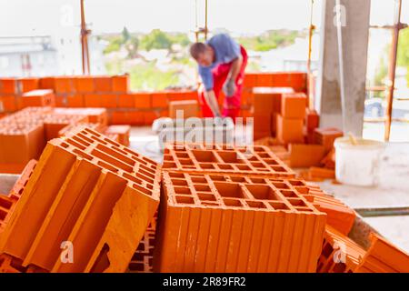 Gros plan sur tas de blocs rouges, en arrière-plan maçon est de construire un mur avec des blocs rouges en céramique en utilisant le mortier d'une gouttière en plastique. Le bâtiment est un Banque D'Images