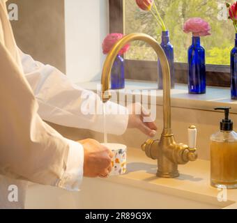 Gros plan des mains dans une cuisine vapeur faire une boisson avec de l'eau à partir d'un robinet d'eau de chaudière Banque D'Images