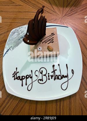 Gâteau d'anniversaire à la truffe servi sur une assiette blanche, avec message d'anniversaire joyeux écrit en chocolat et placé sur une table. Banque D'Images